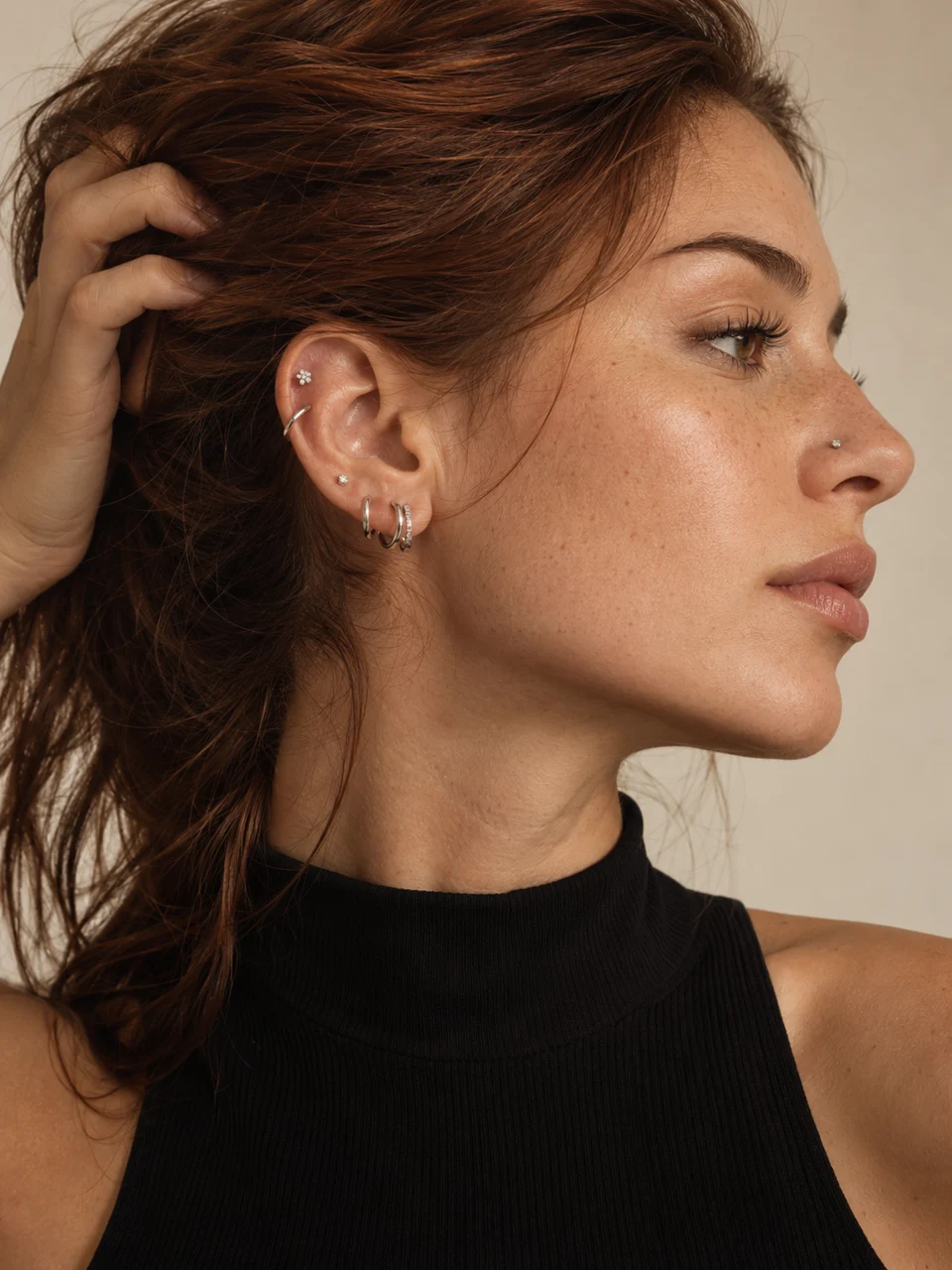 Portrait de profil, cheveux relevés, révélant des anneaux et de délicats bijoux d’oreille.